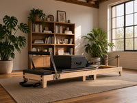 Wood Reformer The Oak Foldable Black Edition, eikenhouten pilates reformer met zwarte bekleding in een sfeervol interieur met boekenkast