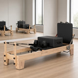 The Oak Studio Black Edition: eikenhouten pilates reformer met zwarte bekleding en rugleuning in een pilatesstudio met spiegelwand
