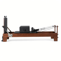 Wood Reformer The Walnut Studio Black Edition – pilates reformer van walnotenhout met zwarte bekleding en rugleuning, zijaanzicht op witte achtergrond