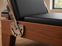 Close-up van de Wood Reformer The Walnut Studio Black Edition: walnotenhouten frame, rvs voetbalkverstelling en zwarte bekleding