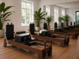 Pilatesstudio met een rij Wood Reformer The Walnut Studio Black Edition reformers van walnotenhout met zwarte bekleding